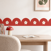 Circus Red daisy scalloped peel-and-stick wallpaper border above a wooden desk with a red mushroom lamp.