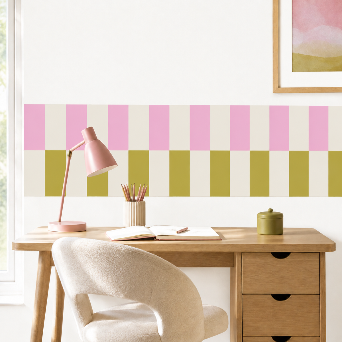 Peel-and-stick checkerboard wallpaper border in pink and olive, styled above a wooden desk with a pink lamp in a modern kids’ room.
