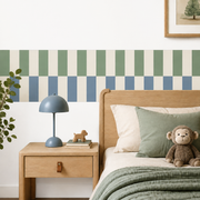 Sage green and dusty blue checkerboard peel-and-stick wallpaper border in a child’s bedroom with a wooden bed and blue lamp.