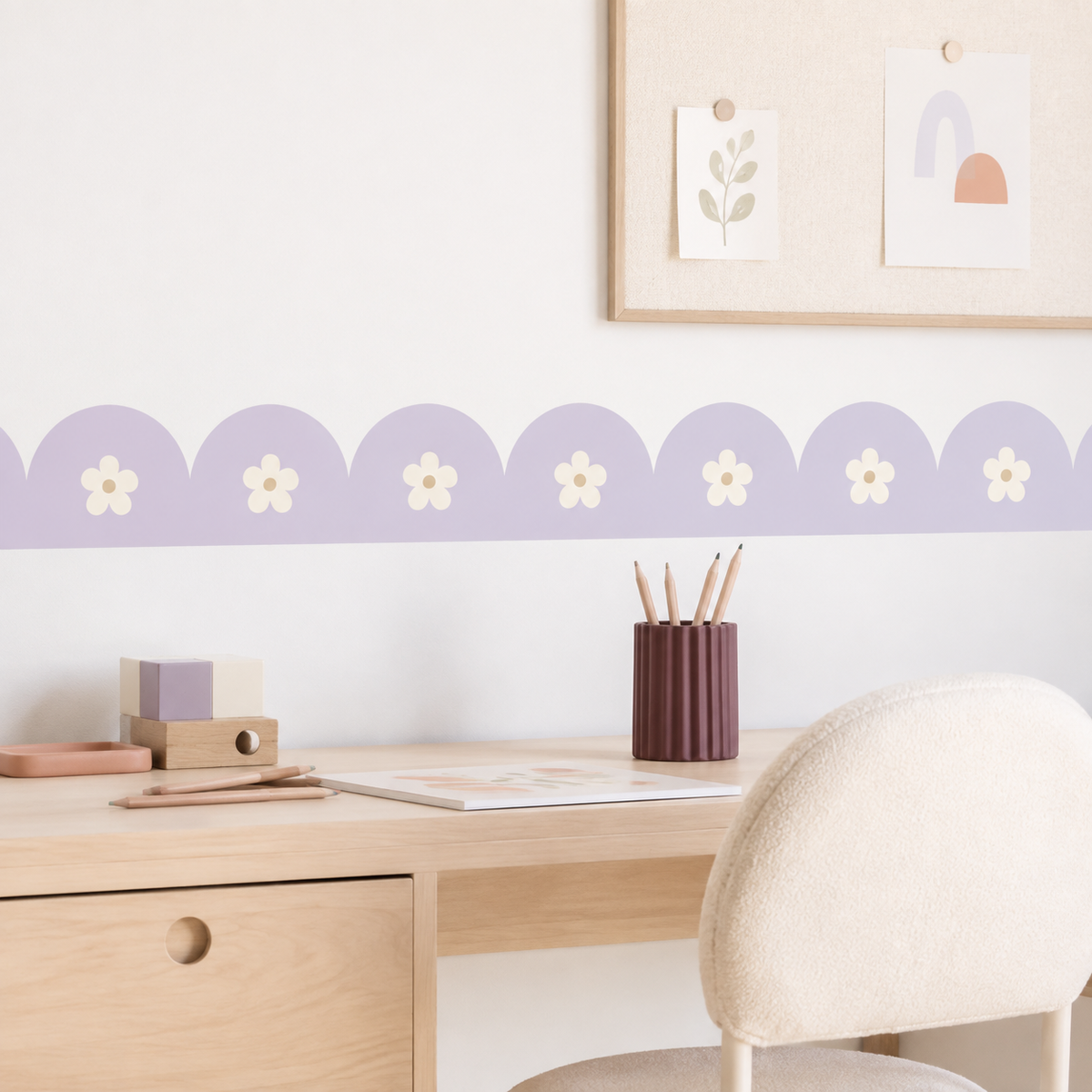 Soft Lilac daisy scalloped peel-and-stick wallpaper border above a wooden desk with a cream chair and pastel accessories.